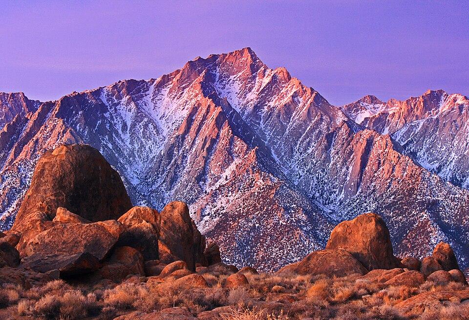 Sunrise light on the snowy Sierra Nevada peaks above the rounded orange boulders of the Alabama Hills in California